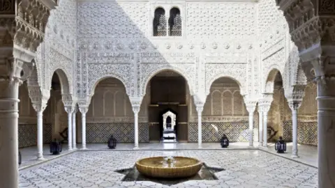 A courtyard with tiled floor, fountain and white ornately carved walls