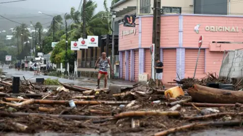 Getty Images Pedestrians stand next to debris and vegetation on a road in Saint-Paul de La Reunion, on the French overseas Indian Ocean island of La Reunion, 