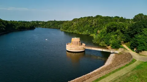 Max Burnett A drone shot of Queen's Valley reservoir. A large body is visible, with the reservoir track and trees pictured in the surrounding area. 
