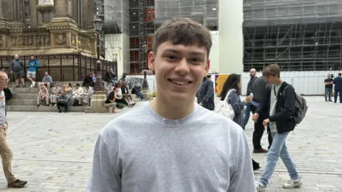 A young man with brown hair and a grey t-shirt.