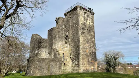 The ruins of an old castle, on top of a hill with part of Glasgow spreading behind it