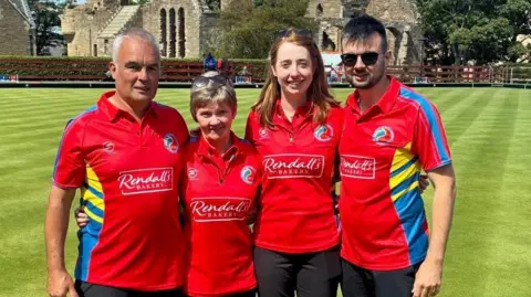 Group of four people standing with bowling green in background.