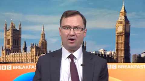 Middle aged man wearing rectangular glasses and a burgundy tie