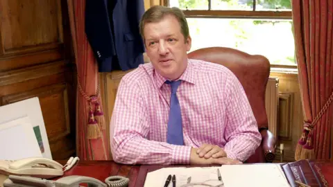PA Media David Murray pictured at his desk in his Edinburgh office in 2002. He wears a pink gingham shirt and a purple tie. Documents and pens sit in front of him.