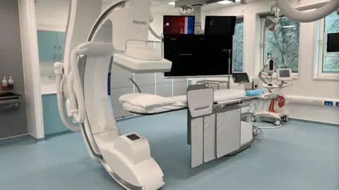 A modern hospital imaging room with a large Philips C‑arm scanner positioned over a patient bed, surrounded by monitors and medical equipment.
