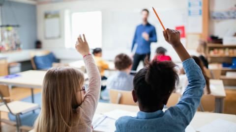 Stock image of two children raising their hand in a lesson