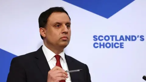 PA Media A man in suit and tie speaks to reporters.