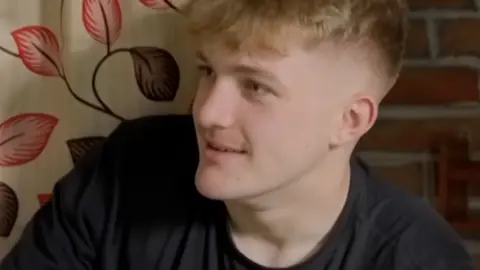 Fin, wearing a black T-shirt and sitting in a hostel room