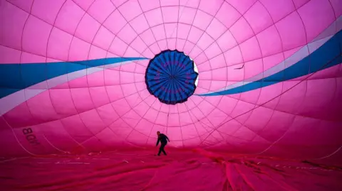 PA Media The inside of a pink hot air balloon which two blue and white stripes. There is a man inside who is slightly ducking. 