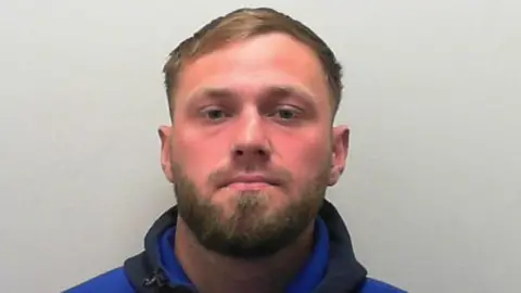 A custody picture of a man with short dark hair and a beard.