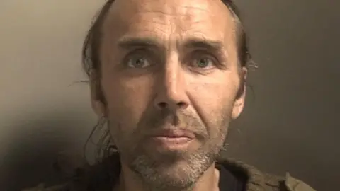 Merseyside Police Glynn has long greying hair pulled away from his face, he has a short beard