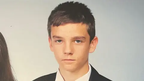 A school photo of Freddie Coleman wearing a black blazer and white shirt. He has short brown hair and is looking at the camera with little expression.
