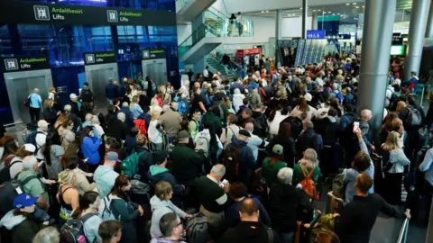 Reuters An overhead shot of a sea of people inside an airport building. There are lifts and departure and arrival boards also visible.