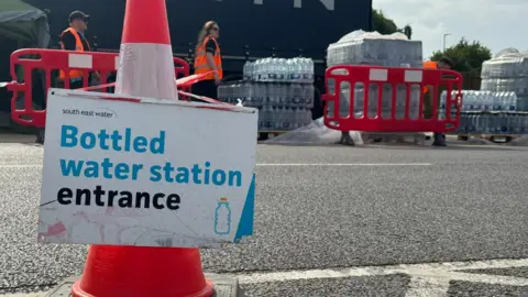 Bottles of water at an emergency outdoor centre in Herne Bay with a sign and cones.