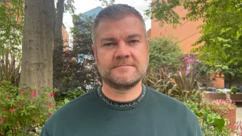 Grey haired and bearded man with a green jumper 