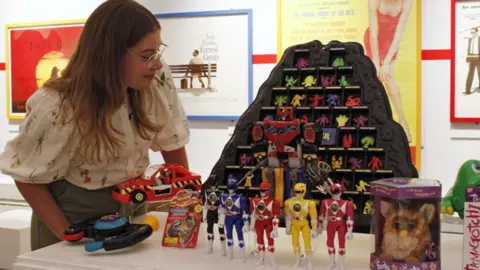 Matt Fox A woman stands and looks at a selection of the toys on display, including Power Rangers, Furby and Tamagotchi. Music posters can be seen in the background.