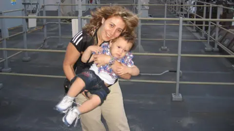 William McCulloch/PA Nadia Ayoub McCullough outdoors with her young son Thomas, aged primary school level. She is holding him in her arms in the air.