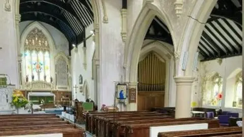 Gareth Simpson/National Churches Trust Rows of wooden pews can be seen inside the church, with the altar at the front and a number of stained glass windows. The walls are cream-coloured with a pillar between one of the rows of pews. 