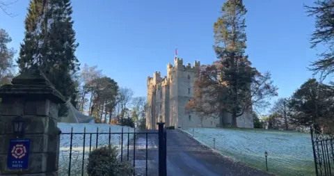 The exterior of Langley Castle. It is a grand, white-stone complex. The field on the front is dusted with snow.