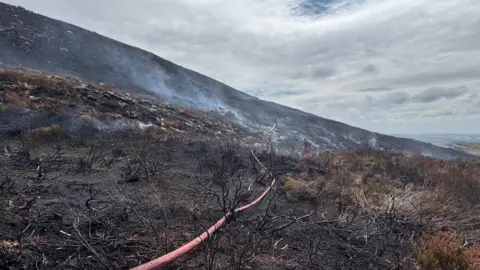 Burnt moorland with a hose and firefighters in the distance