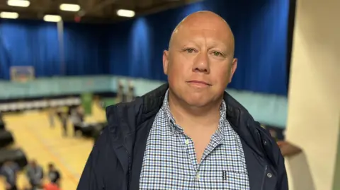 A bald man with a dark blue coat and a checkered shirt.