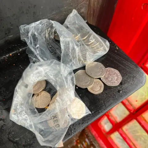 William Arnold Two bags of coins on a shelf in the phone box.