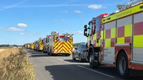 A line of fire engines on the road.