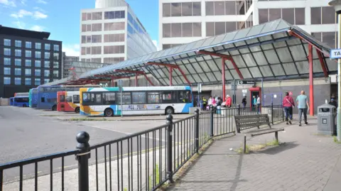 Dave Cox Image of buses lined up at Swindon Bus Station with people walking on the pavements. There are high-rise buildings in the background