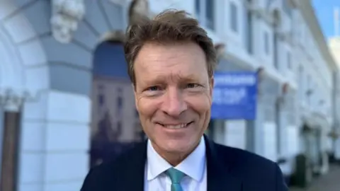 Sharon Edwards/BBC MP Richard Tice smiles as he stands in front of a row of units in Boston. He is wearing a blue tie, white shirt and black blazer.