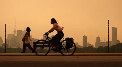Getty Images Thick, yellow smoke blanketed Toronto on Wednesday. a woman on a bike rides through it