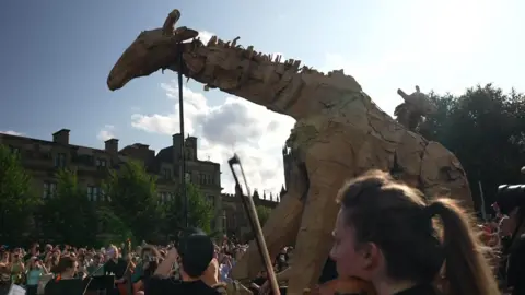 Woman plays violin next to a wooden giraffe