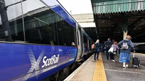 Several passengers walking along a platform next to a ScotRail train
