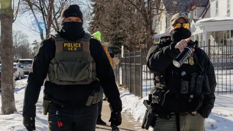 Anadolu via Getty Images US Immigration and Customs Enforcement (ICE) agents wearing black masks conduct immigration enforcement operations in Minneapolis.