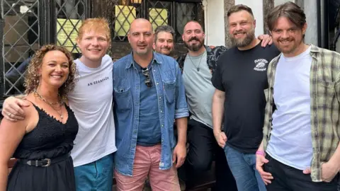 A group of people, including pop artist Ed Sheeran standing outside an old school pub 