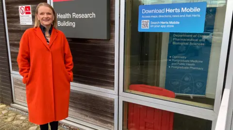 A picture of a woman in a bright orange jacket outside a building in Hatfield, Hertfordshire.