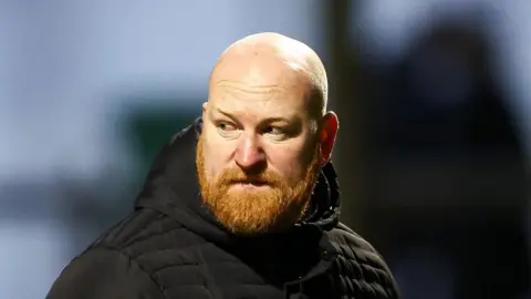 Andy Whing, wearing a big puffer coat, looking back over his shoulder 