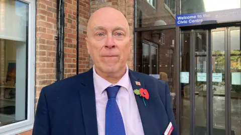Reform Councillor Rob Wharton is wearing a blue suit with a pink shirt, and a blue tie.