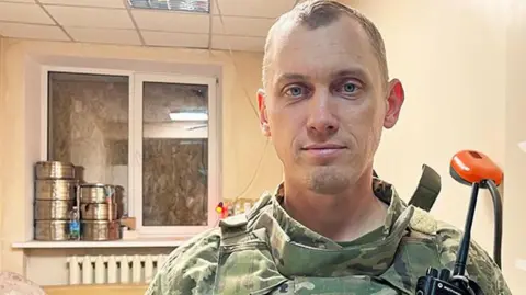 Imogen Anderson/BBC Oleksandr, the head of a medical unit for the Ukrainian army's 25th brigade, photo'd at his place of work, wearing army uniform, and facing the camera in a bare-looking room