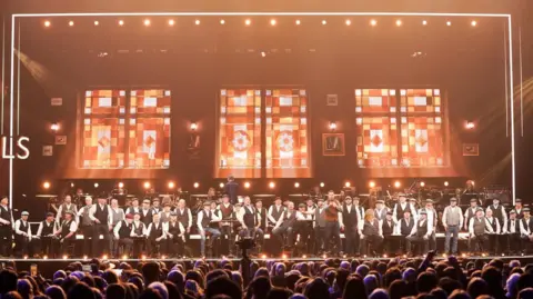 National Lottery The full choir of Infant Hercules performing on stage alongside TV star and host Jason Manford.