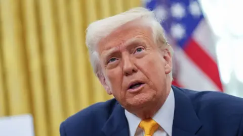 A close-up US President Donald Trump in the Oval Office with the US flag behind him