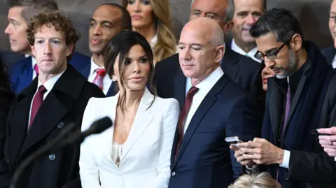 From left to right: Meta CEO Mark Zuckerberg wearing a navy suit, red neck tie and white dress shirt; Lauren Sanchez, wife of Amazon founder and former CEO Jeff Bezos, wearing a white blazer; Jeff Bezos, in a navy suit, red neck tie and white dress shirt; Google CEO Sundar Pichai, in an all black coat, shirt and tie.