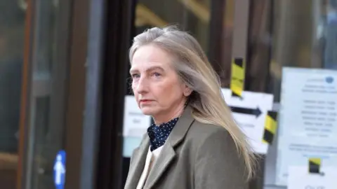 Spindrift A 59-year-old woman with long blonde hair, wearing a light green blazer and a checked scarf, leaves a court building