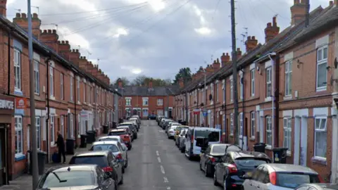 Google A terraced street with cars parked either side of the road 