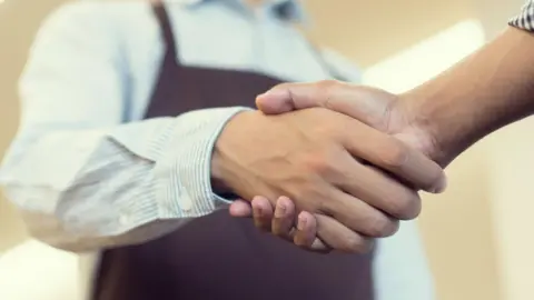 Close up of somebody wearing cafe overalls shaking hands with a customer