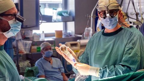 Image of doctor holding the shockwave device while in surgery environment wearing scrubs, face mask and gloves