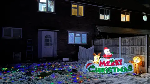 The back of a house with snow on the lawn, which is also covered with Christmas lights