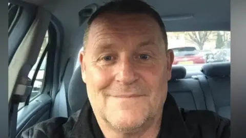 A man in a black jacket sitting inside a car.