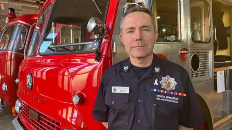 A man in uniform standing in front of a vintage fire engine.