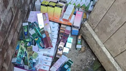 A police picture of dozens of boxes of cigarettes and vapes, in various colours, stored in an outbuilding