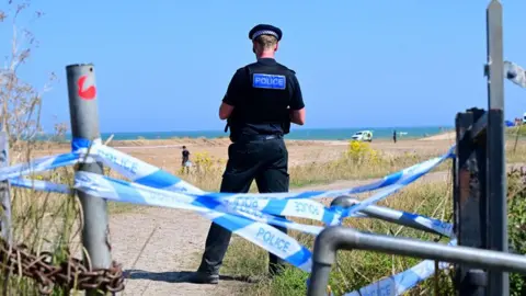 Shutterstock Police patrol the scene near Warden Bay beach after the death of man on Isle of Sheppey on 11 August 2025